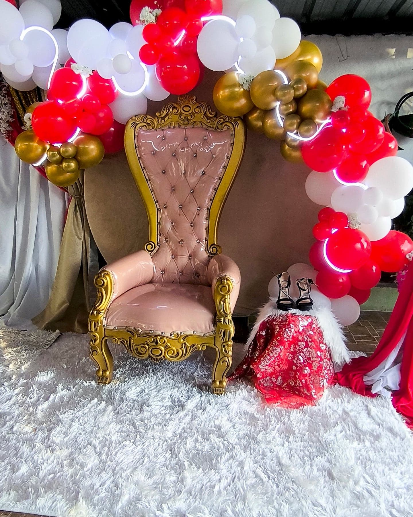 Trono rosado y dorado entre globos rojos, blancos y dorados